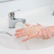 Bild von eingeseiften Frauenhänden über einem weißen Waschbecken, mit Wasserhahn und Seifenspender