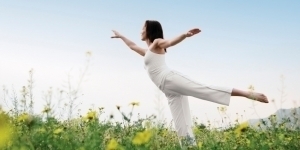 Bild einer weiß gekleideten, yogaausübenden Frau auf einer gelben Blumenwiese