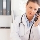Foto einer Ärztin im Büro mit Stethoskop um den Hals telefoniert und sieht auf einen Computerbildschirm
