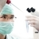 Doktor in türkiser Kleidung mit Mundschutz und weißen Handschuhen träufelt etwas in eine Phiole