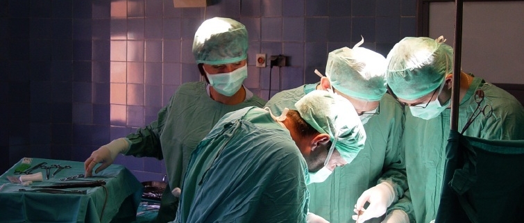 Vier Ärzte in türkisen Kitteln und Mundschutz bei einer Operation im OP-Saal