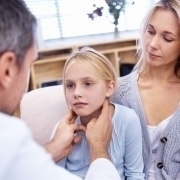 Arzt tastet krankes Mädchen, neben ihrer Mutter sitzend, am Hals ab