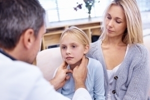 Arzt tastet krankes Mädchen, neben ihrer Mutter sitzend, am Hals ab