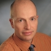 Portrait of Dr. Thomas Hauer in a orange shirt and grey tie