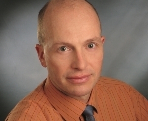 Portrait of Dr. Thomas Hauer in a orange shirt and grey tie