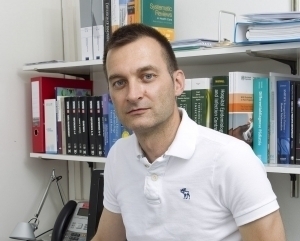Portrait of Dr Walter Zingg in a white shirt in his office, bookshelves in the back